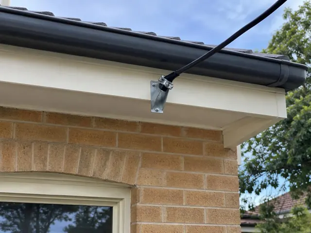 Overhead service cable and point-of-attachment bracket on a brick house exterior in Killara